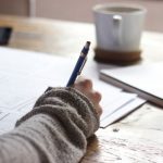 User Content - person writing on brown wooden table near white ceramic mug