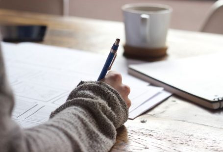 User Content - person writing on brown wooden table near white ceramic mug