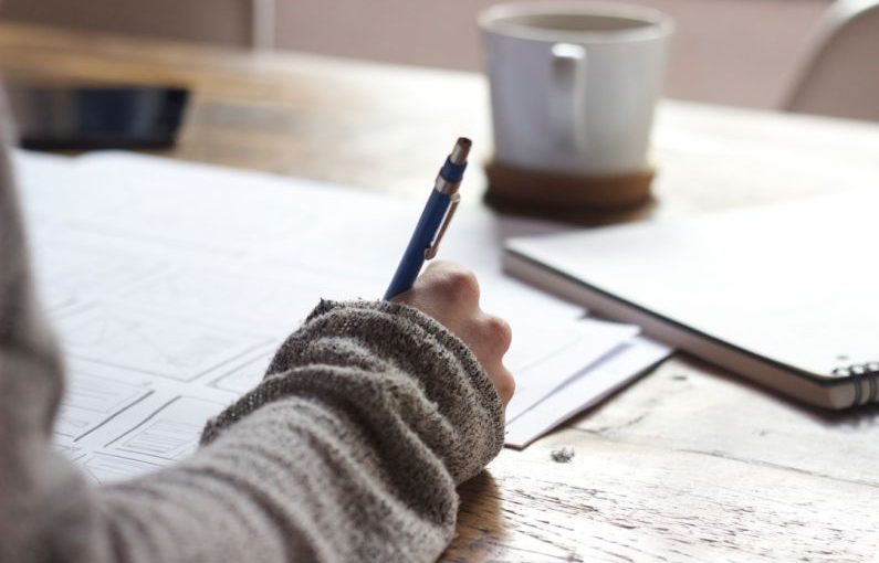 User Content - person writing on brown wooden table near white ceramic mug