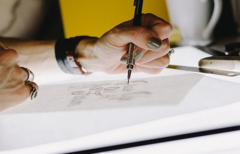 Logo Design - person lettering on tracing paper using mechanical pencil